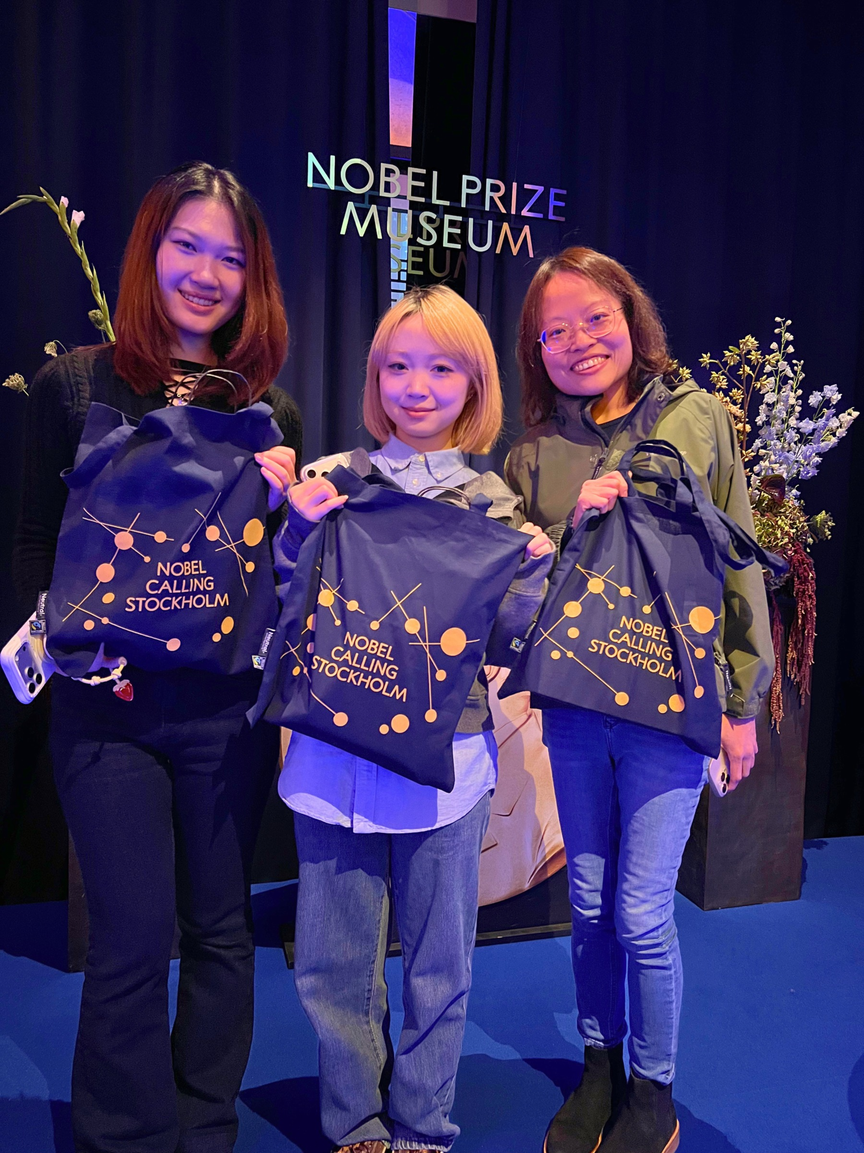 Three students holding Nobel Calling Stockholm bags at the Nobel Prize Museum following the welcome reception.